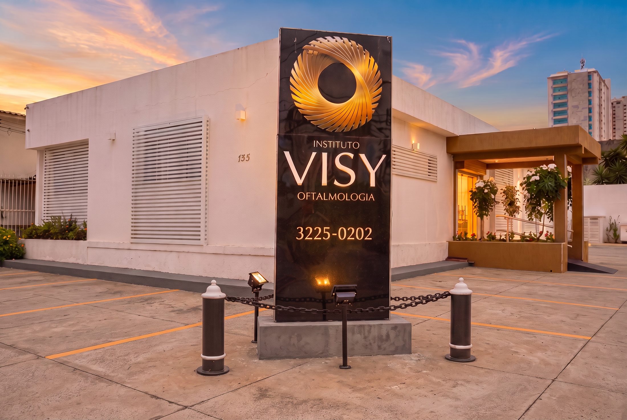 Fachada do Instituto VISY em Goiânia ao entardecer, com totem preto e o símbolo dourado